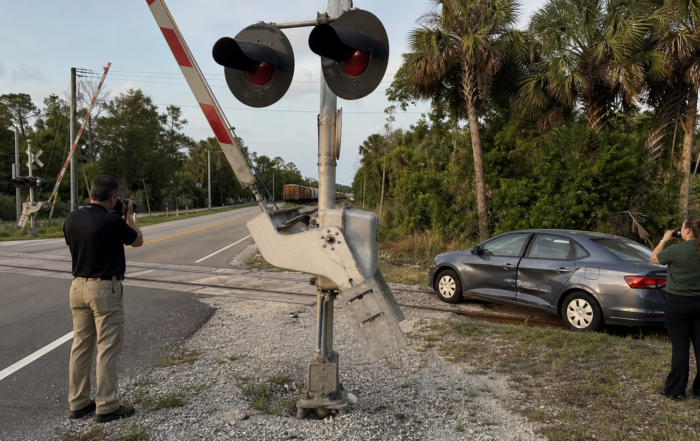 Railroad crossing accident claim scene with investigators, a damaged car, and crossing equipment